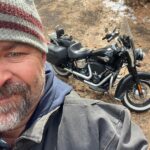 A man in a hat and jacket next to a motorcycle.